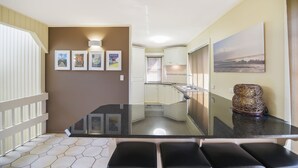 Una cocina moderna con armarios blancos, un lavamanos de acero inoxidable y un comedor con mesa de vidrio y sillas negras.