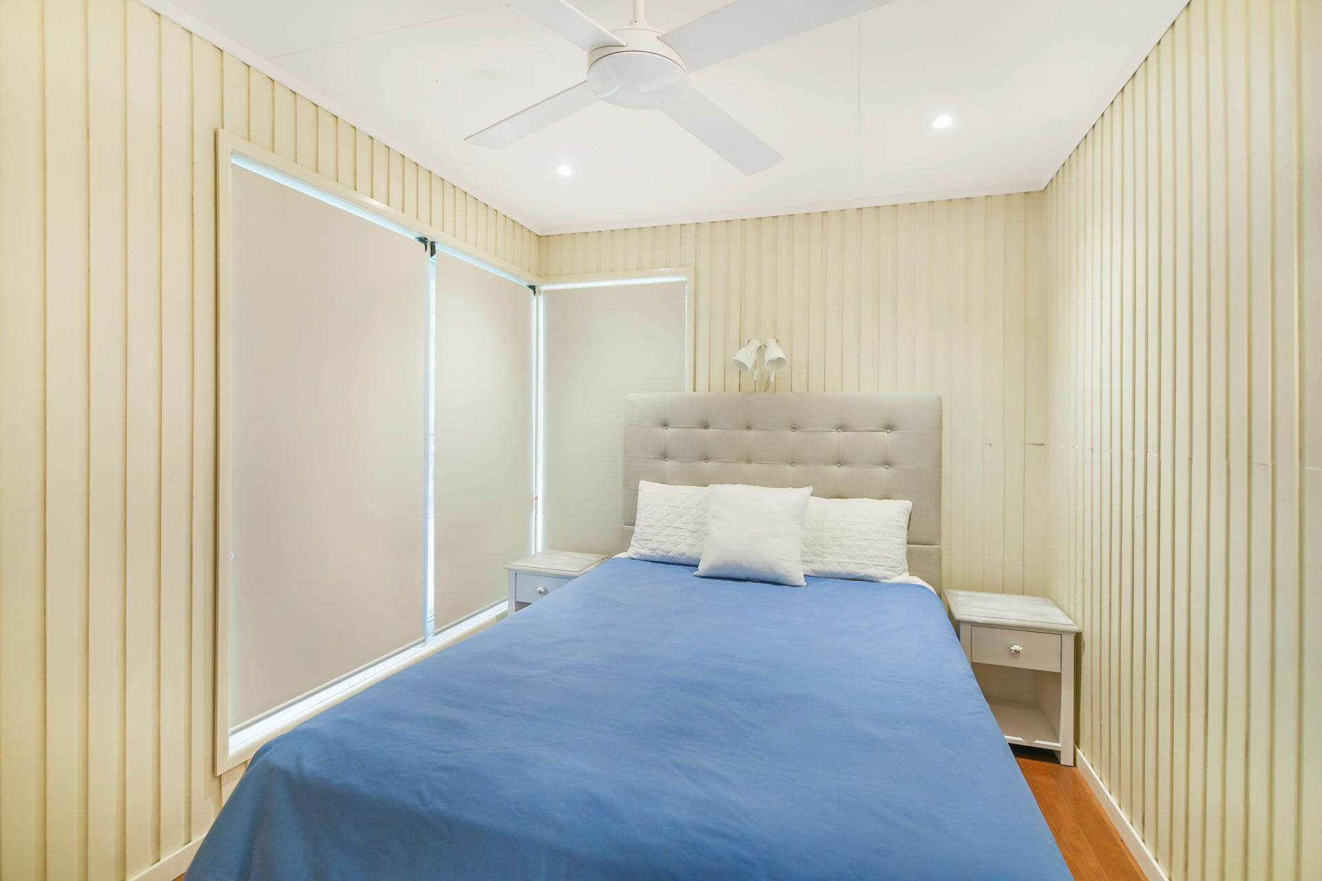Une chambre à coucher avec un lit, des tables de chevet, un ventilateur de plafond et des stores verticaux.