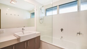 Un baño moderno con ducha envuelta en vidrio, un espejo grande y un lavamanos blanco.