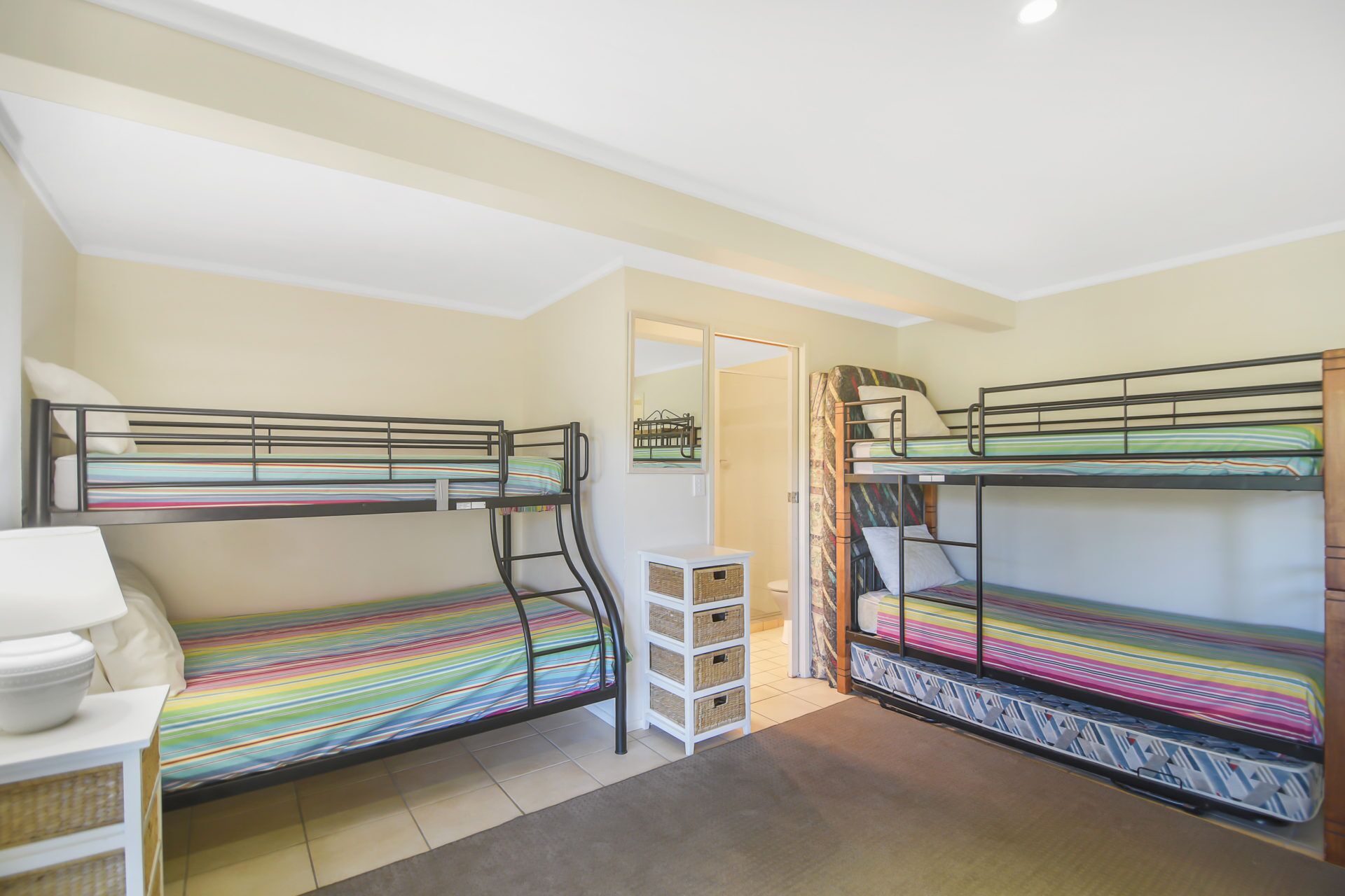 A dormitory room with bunk beds, a small white cabinet, and a mirror on the wall.