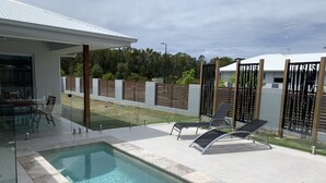 A swimming pool with lounge chairs, a glass enclosure, and a view of the surrounding area. - Pet Friendly, new House Peregian Breeze Drive, Peregian Beach (Peregian Beach)