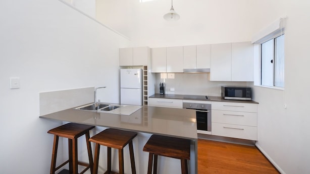 Een moderne keuken met een centraal eiland, barkrukken, een magnetron en een koelkast.