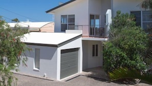 Een tweelaags huis met een garage, een balkon en een helderblauwe lucht.