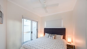 Een slaapkamer met een bed, een plafondventilator, een nachtkastje met lamp en een schuifdeur met glas.