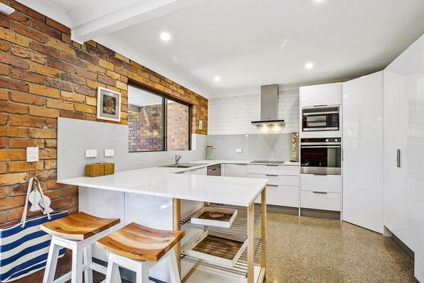 A modern kitchen with white cabinets, a brick accent wall, and a built-in oven.