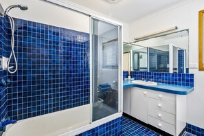 A bathroom with blue-tiled walls, a glass shower enclosure, a white sink, and a mirror.