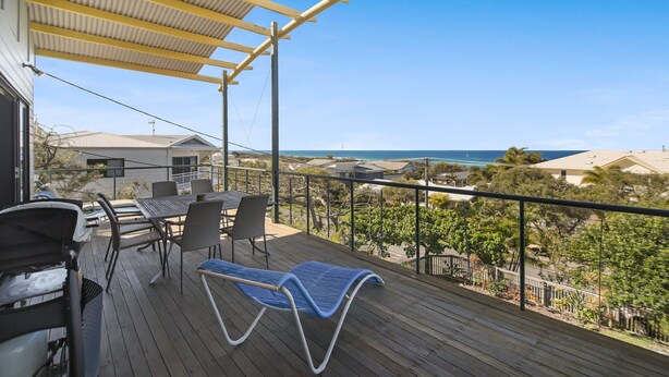 A wooden deck with a table and chairs, overlooking a coastal area with houses and a view of the ocean. - Peregian Beach House - 2/22 Avocet Parade (Peregian Beach)