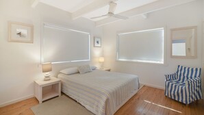 A bedroom with a bed, bedside tables, a ceiling fan, a window, and a striped chair. - Peregian Beach House - 2/22 Avocet Parade (Peregian Beach)