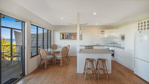 A modern kitchen with a central island, white cabinetry, and a dining area with wicker chairs. - Peregian Beach House - 2/22 Avocet Parade (Peregian Beach)