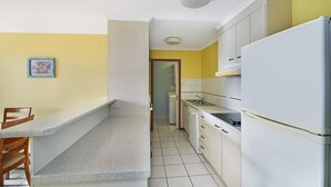Una cocina compacta con armarios blancos, horno integrado y un lavamanos. Hay un pequeño comedor con una silla y una mesa.