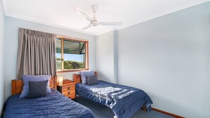 Un dormitorio con dos camas, una ventana con cortinas, un ventilador de techo y vistas a zonas verdes.
