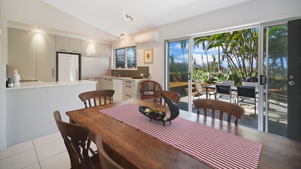 A modern kitchen with a dining area and a sliding glass door leading to a tropical garden. - Nobs -1/44 Peregian Esplanade (Peregian Beach)