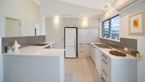 A modern kitchen with white cabinetry, a central island, a built-in oven, and a window with a view. - Nobs -1/44 Peregian Esplanade (Peregian Beach)