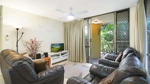 A living room with a sofa set, a TV, a floor lamp, and a sliding glass door leading to a balcony.