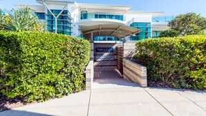 A modern building with a covered entrance, a sign reading "Perregian on the Beach," and a well-maintained hedge.
