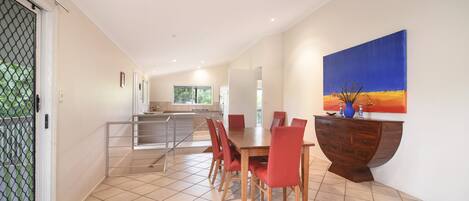 A spacious dining area with a long table and red chairs, a wooden cabinet with drawers, and a large painting on the wall.