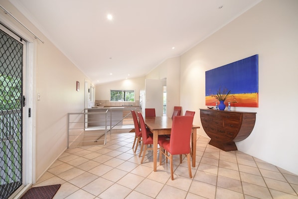 A spacious dining area with a long table and red chairs, a wooden cabinet with drawers, and a large painting on the wall.