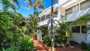 Un patio con camino de ladrillo, palmeras y un edificio de fachada blanca y balcones.