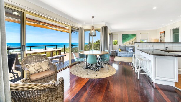 A spacious living area with a view of the ocean, a dining table, and a kitchen area.
