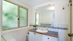 A bathroom with a white sink, a mirror, and a window with a metal screen.