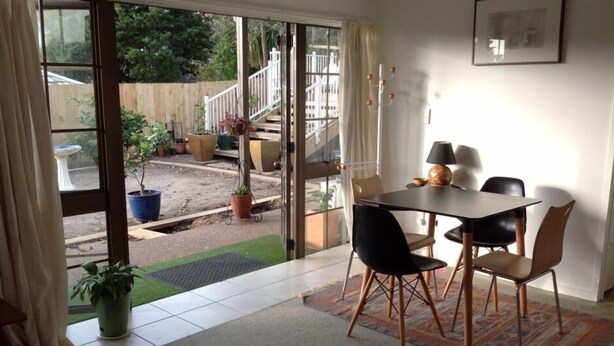 Een eetgedeelte met een tafel en stoelen, een potplant en uitzicht op een houten terras en trap.