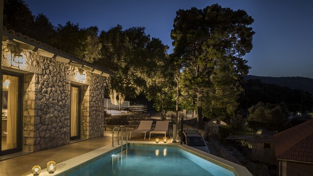Une piscine extérieure avec des murs en pierre, deux chaises longues et un bâtiment en pierre illuminé.