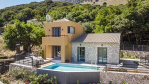 Une maison moderne à deux étages, dotée d’une piscine, d’une façade en pierre et offrant une vue sur une colline boisée.