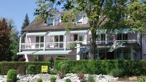 A two-story building with a balcony, a sign indicating a restaurant, and a landscaped garden with rocks and plants. - Hotel Iris am See (Radolfzell am Bodensee)