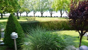 A well-maintained garden with a variety of plants, a metal sculpture, and a view of a body of water in the background. - Hotel Iris am See (Radolfzell am Bodensee)