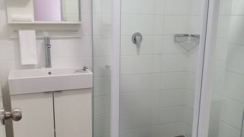 Un baño con ducha envuelta en vidrio, un lavamanos blanco y un inodoro.