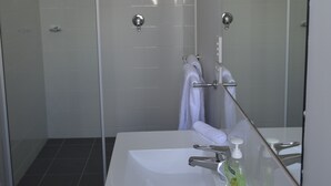 Casa de banho moderna com lavatório branco, cabine de duche em vidro e um espelho grande.