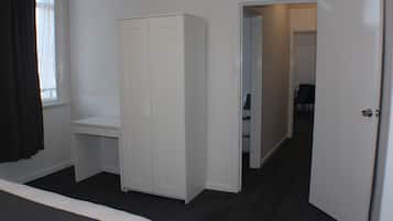 A bedroom with a bed, a white wardrobe, a desk, and a door leading to another room.