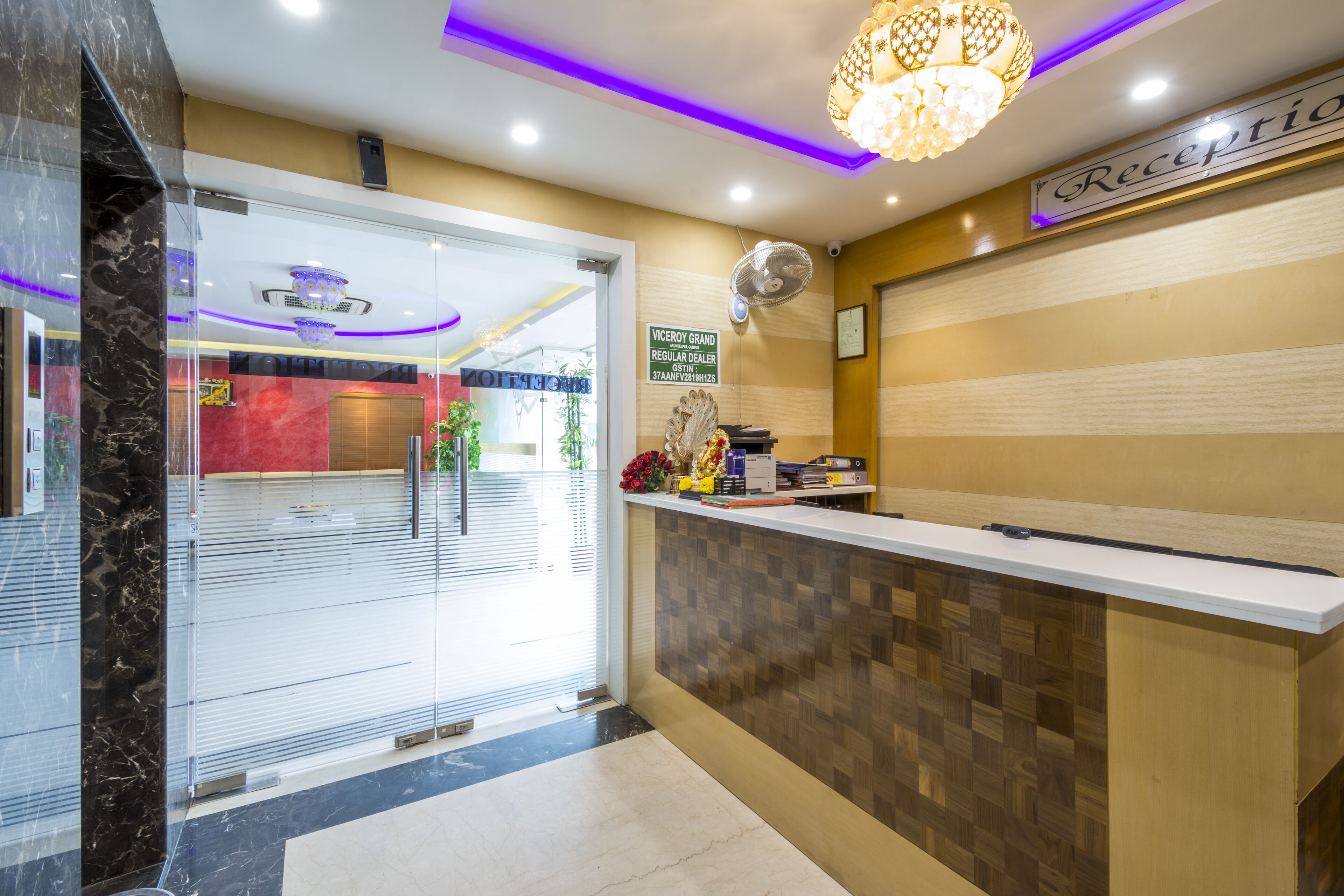 A reception area with a reception desk, a sign indicating the location, a fan, and a chandelier.