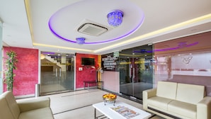 A hotel lobby with a reception desk, a sofa, a coffee table with a newspaper, and a decorative bowl of flowers. - Ostin Viceroy Grand (Guntur)