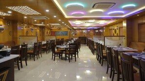 A spacious restaurant with multiple dining tables and chairs, a polished floor, and modern ceiling lighting. - Ostin Viceroy Grand (Guntur)