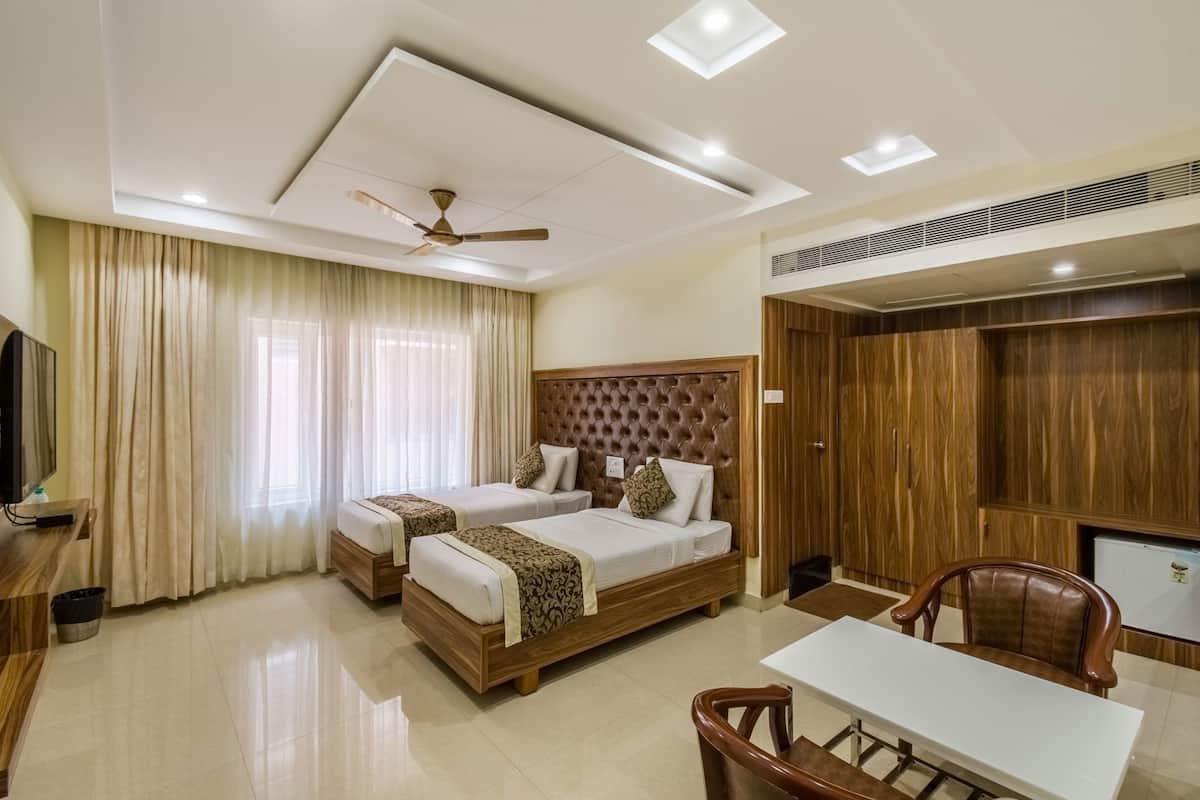 A hotel room with two beds, a desk, a chair, a ceiling fan, and a wardrobe.