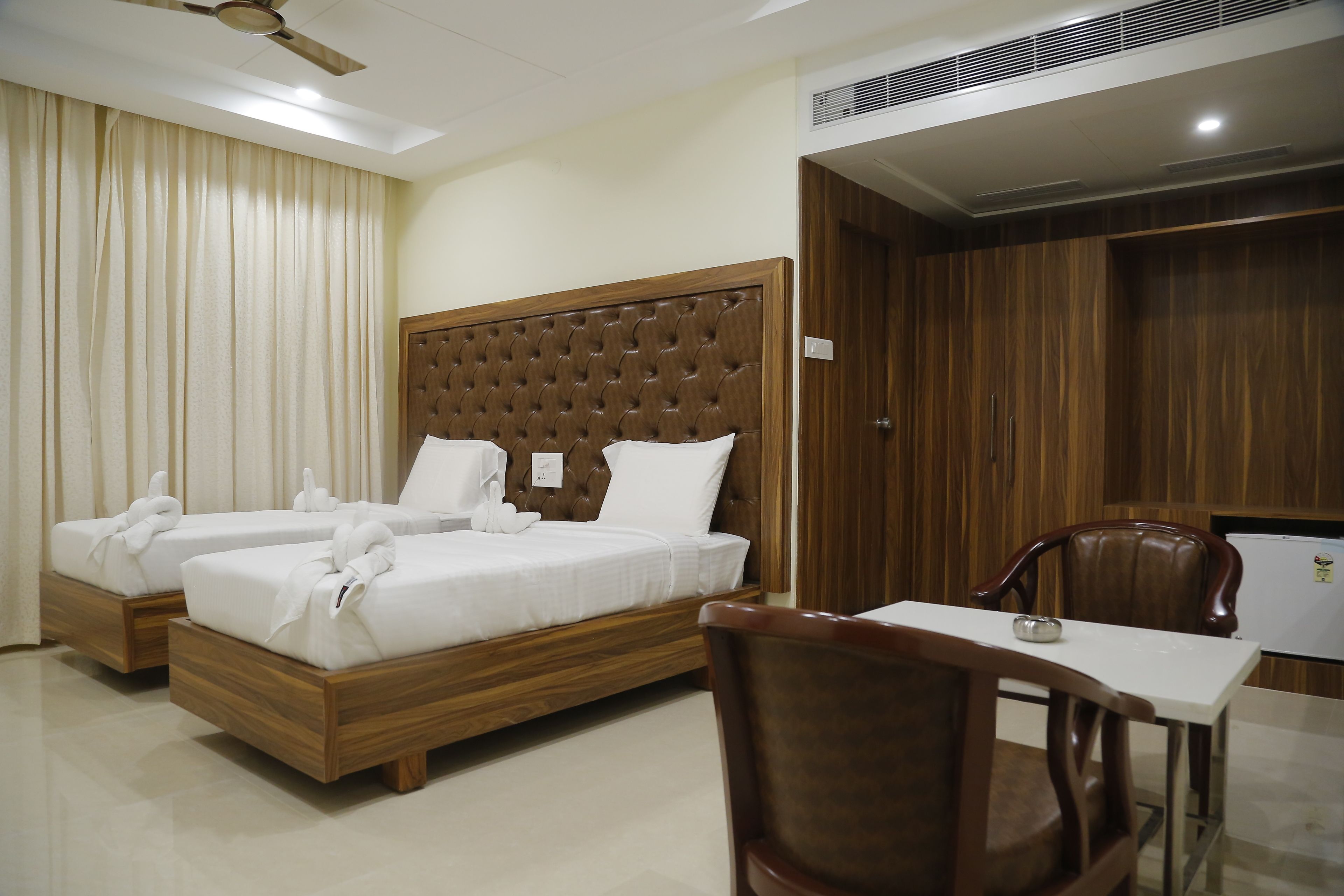 Ein Hotelzimmer mit einem großen Bett, zwei Einzelbetten, einem Holzkopfende, einem Tisch und einem Stuhl.