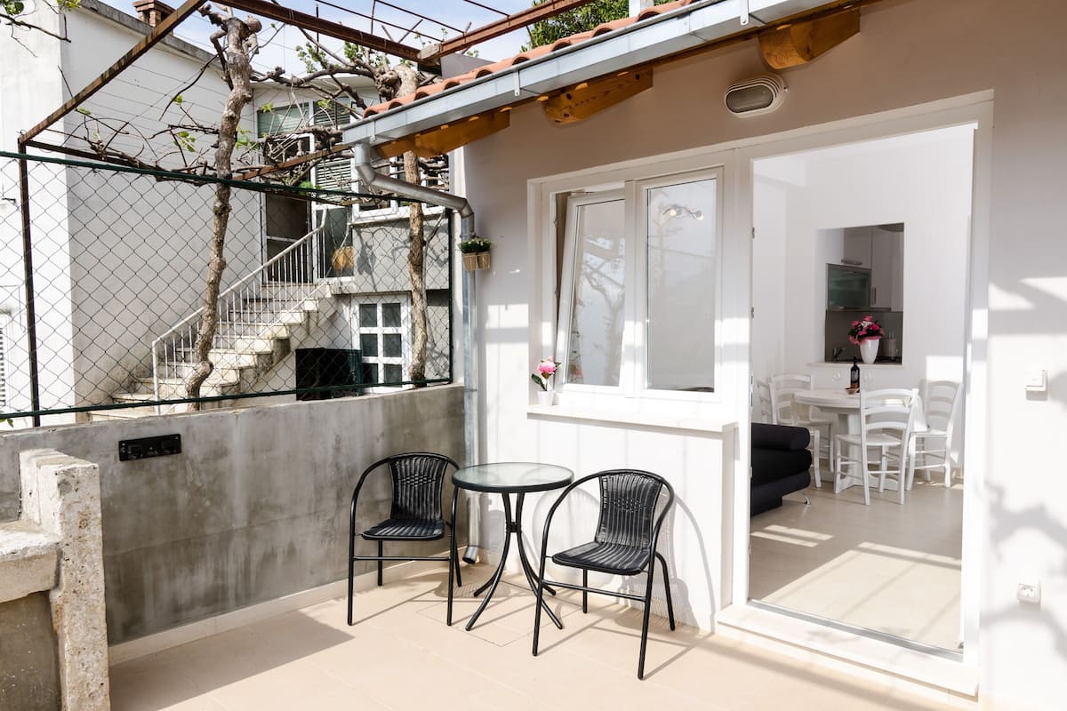 A balcony with a table and chairs, a view of a staircase, and a glimpse of a dining area.