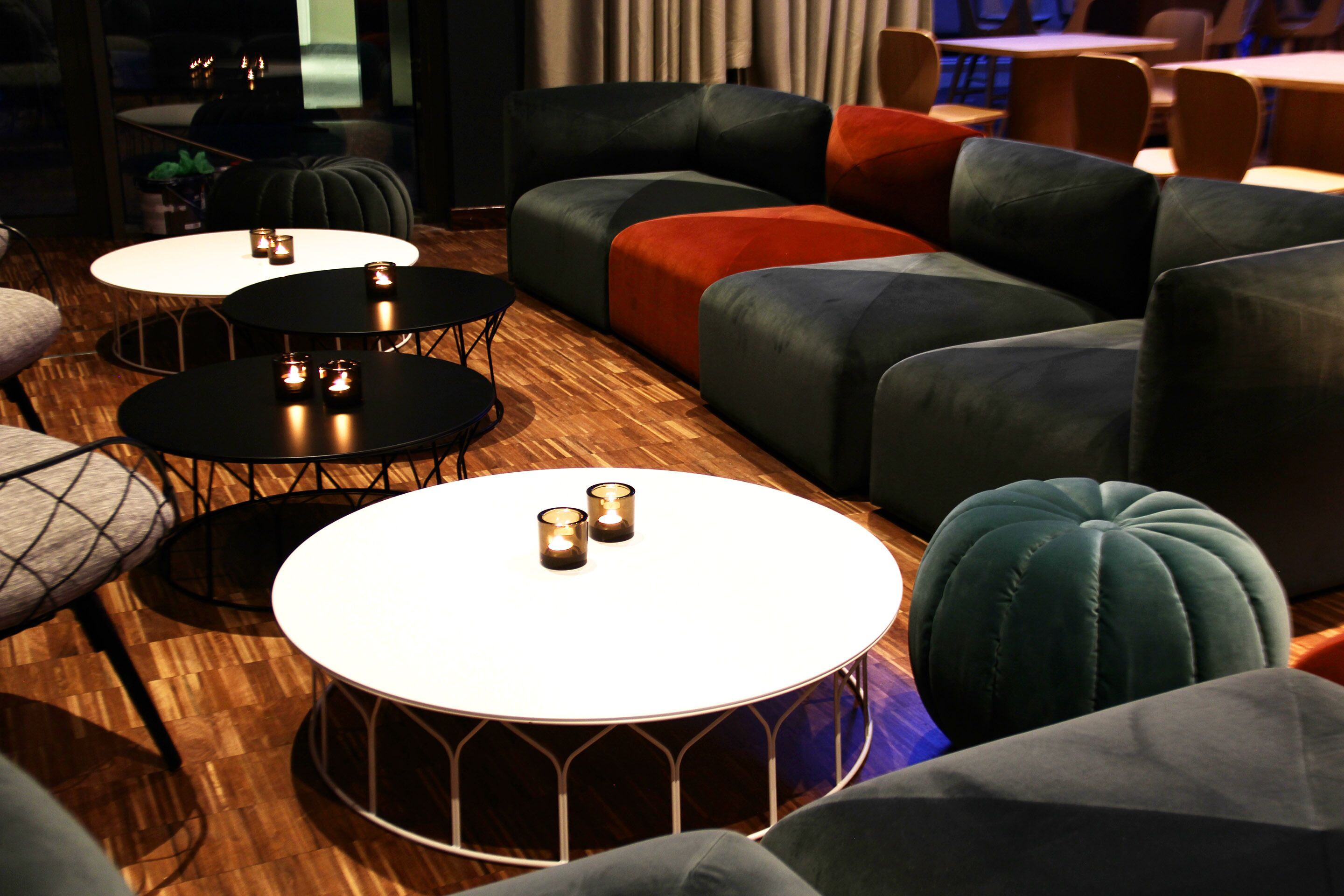 A modern lounge area with round tables and sofas, featuring a wooden floor and ambient lighting.
