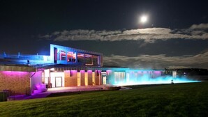A modern house with a pool, illuminated by colorful lights, under a night sky with a visible moon. - Cape East (Haparanda)