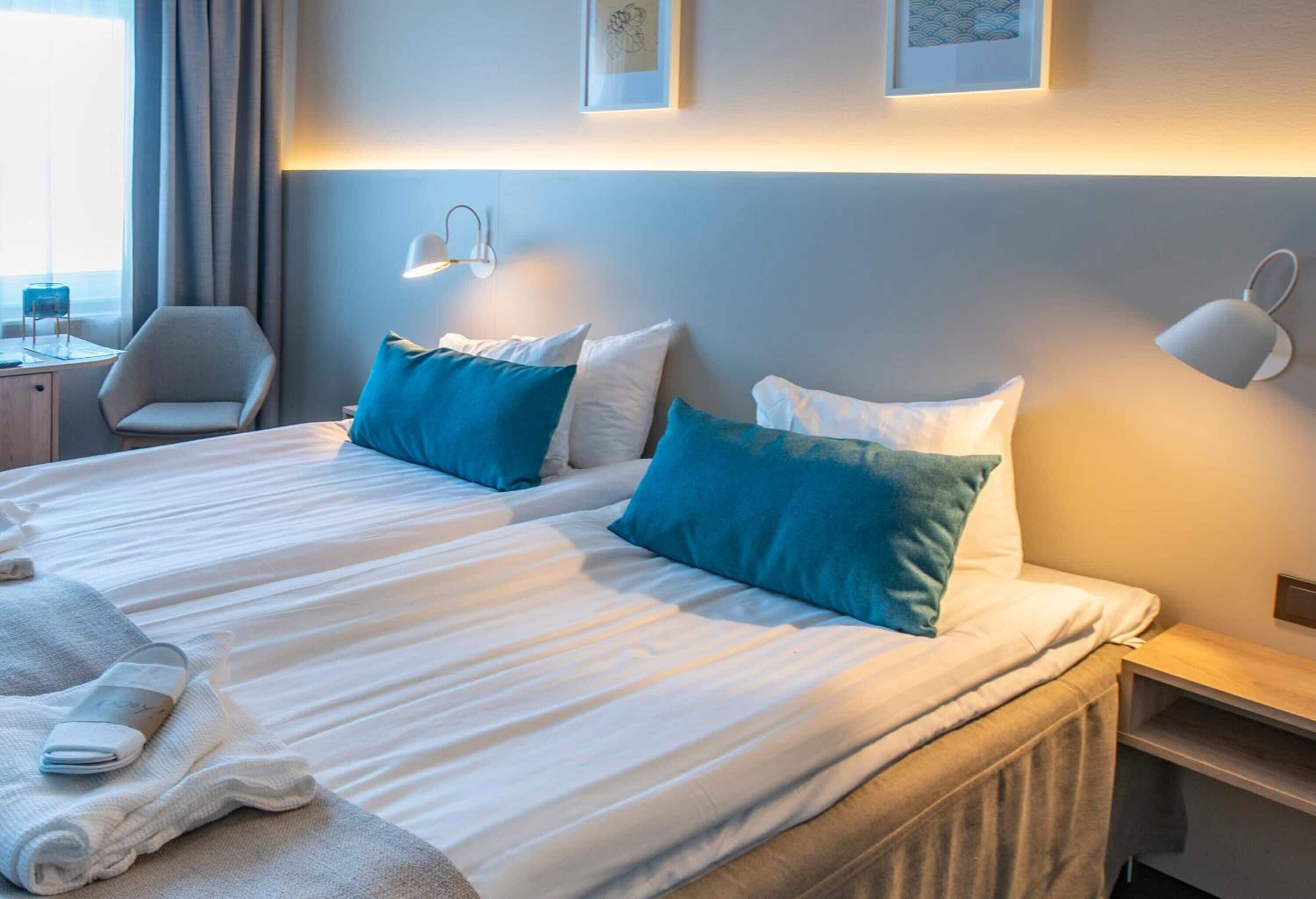 A hotel room with a large bed, two pillows, a bedside table, a chair, and a lamp.