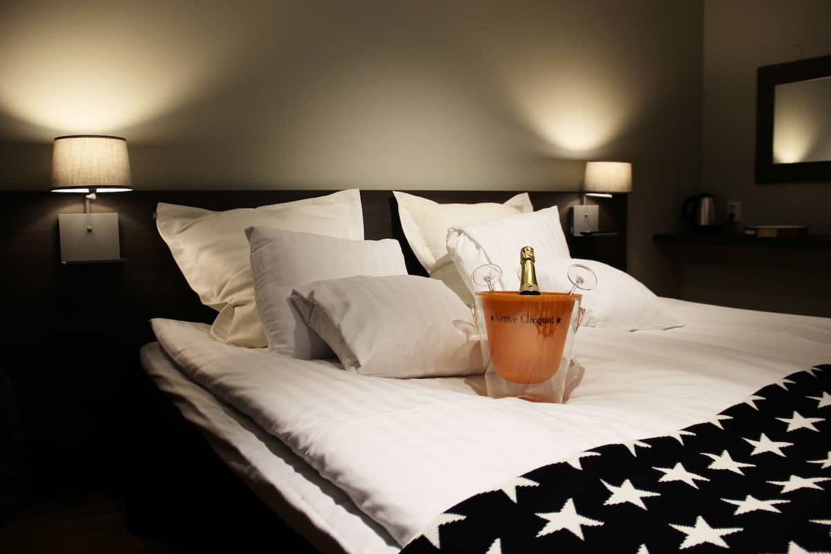 Una cama bien hecha con sábanas blancas, una manta con estampado de estrellas en blanco y negro y una botella de champán sobre las almohadas.