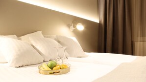A neatly made bed with white linens, a tray of fruit, and a wine glass set on the side. - Cape East (Haparanda)