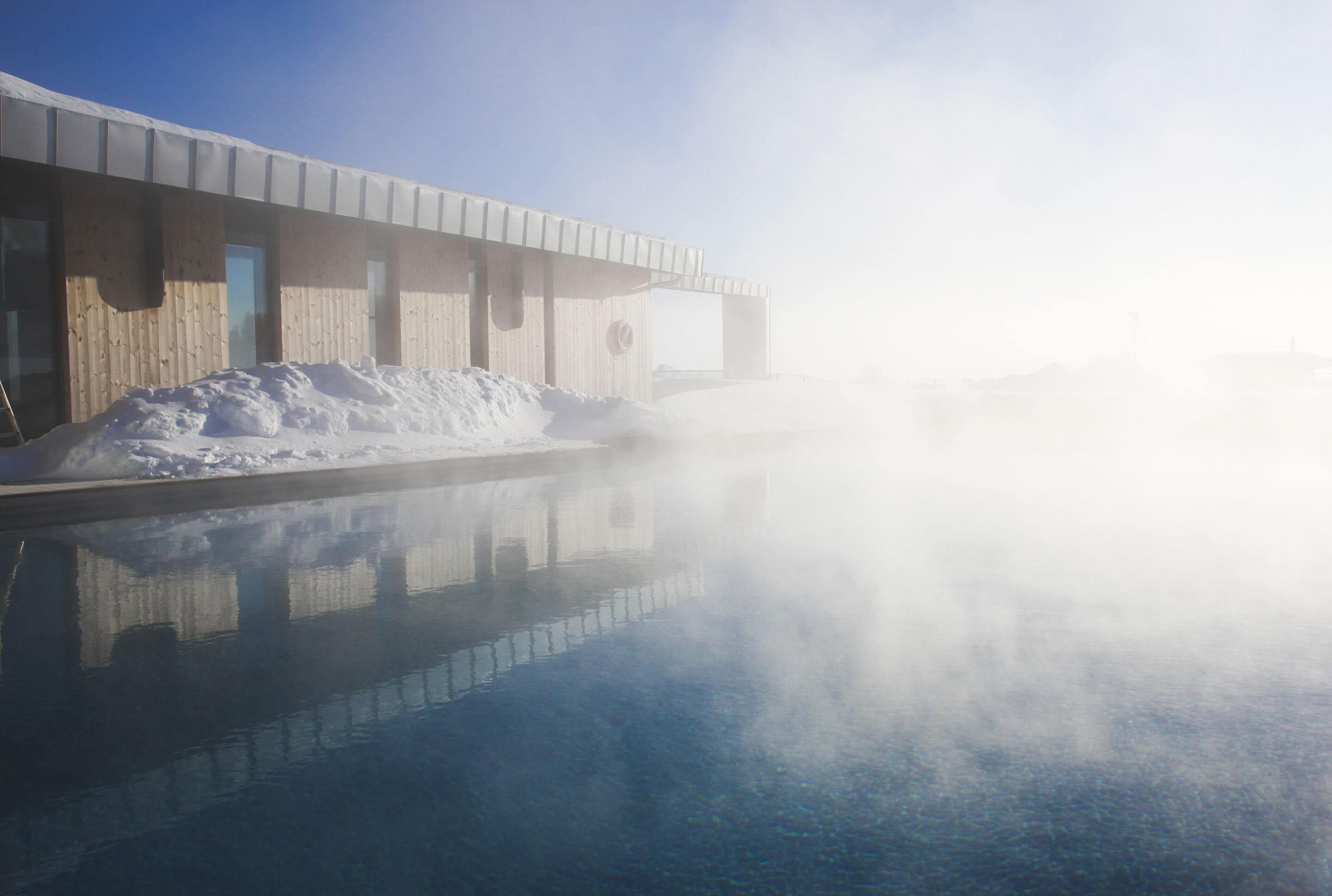 A modern building with a reflective pool and a snow-covered area in front.