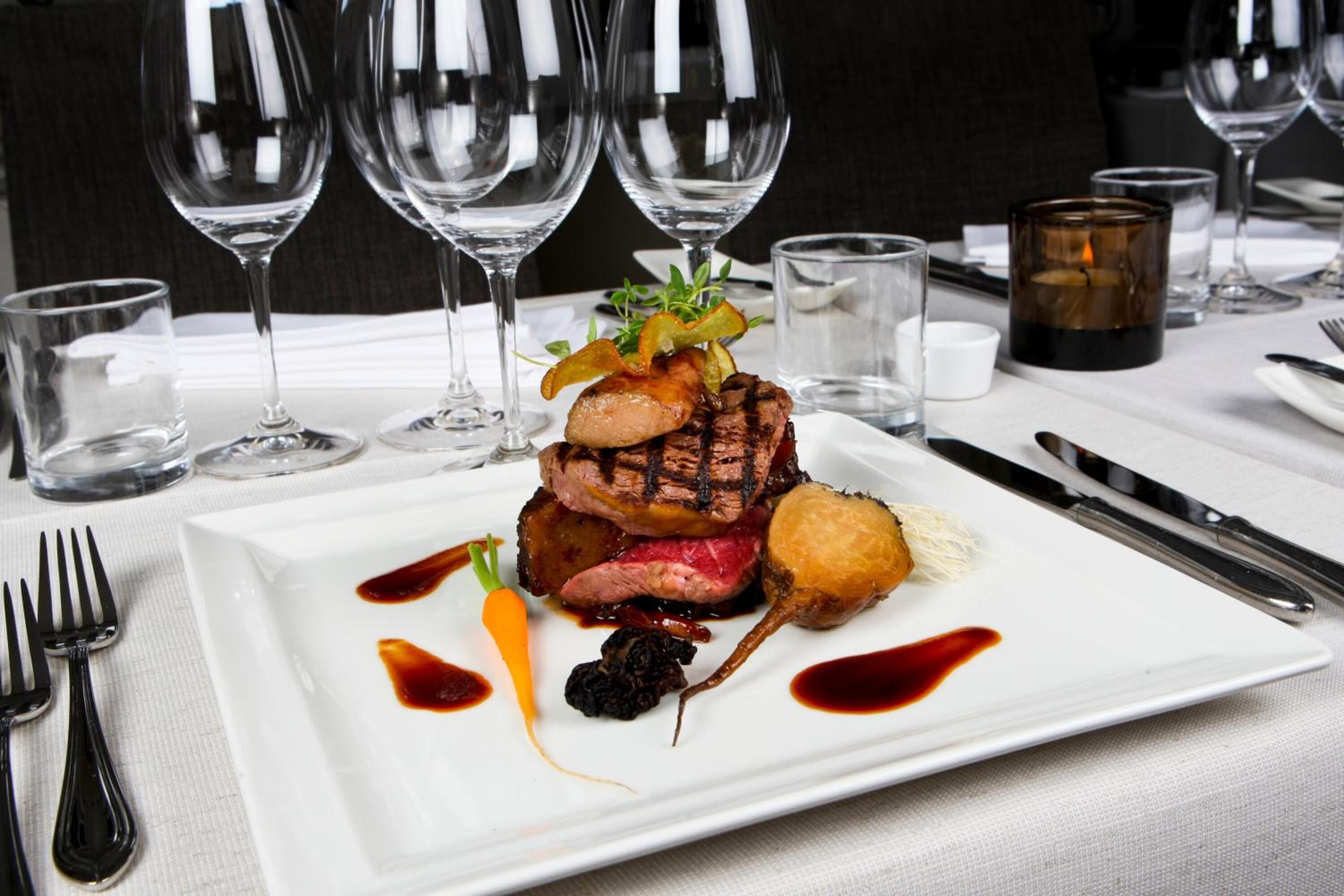 A plated dish with a variety of food items and sauces, accompanied by wine glasses and cutlery on a table.