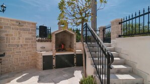Un espacio al aire libre con paredes de piedra, una parrilla, un árbol pequeño y una escalera con barandilla de metal.