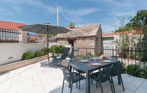 Une terrasse extérieure avec une table dressée pour le repas, entourée de chaises et d’un parasol.