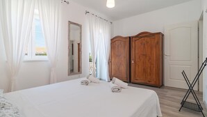 Un dormitorio con cama, armario, espejo y ventana con cortinas.