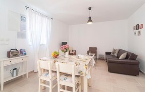 A well-lit living room with a dining area, a brown sofa, a table with a floral tablecloth, and a radio on a shelf. - 2 bedroom nice home in Primosten (Primosten)