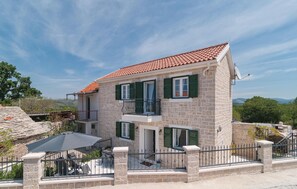 Une maison en pierre à deux étages, avec un toit recouvert de tuiles rouges, des volets verts et un balcon doté d’une balustrade noire.